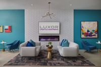 Luxor Lifestyle Apartments lounge area showcasing modern furniture, vibrant artwork, and a sleek wall fireplace in a stylish teal and white setting.