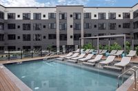 Contemporary apartment complex with a luxurious outdoor pool area featuring stylish lounge chairs and a pergola, perfect for relaxation and leisure.