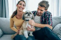 Happy couple sitting on a cozy sofa in a bright living room with their adorable dog, enjoying a relaxed and joyful atmosphere.