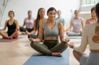 Group yoga class with smiling individuals in a serene, well-lit studio, focusing on mindfulness and relaxation.