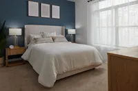 Apartment bedroom with upholstered bed, white bedding, blue accent wall, nightstands, and natural light.