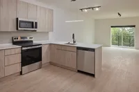 Open kitchen in an unfurnished apartment with light wood cabinets, stainless steel appliances, white countertops, and balcony view.