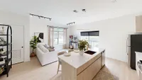 Bright and airy living space with stylish open kitchen, modern appliances, and cozy lounge area with a large window view.