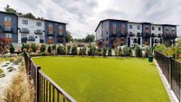 Modern apartment complex with stylish exterior and beautifully landscaped grounds featuring lush greenery and open spaces.