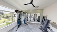 Modern fitness center with state-of-the-art equipment, including a weight rack, cable machine, and large mirrors, overlooking scenic greenery through expansive windows.
