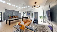 Luxurious and spacious apartment interior with modern decor, featuring a stylish leather sofa, chic black armchairs, elegant lighting, a large TV, and a sleek billiards table in an open-concept living area.