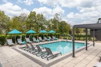Inviting outdoor pool area with sleek lounge chairs and vibrant blue umbrellas, set against a lush green backdrop, perfect for relaxation and enjoyment.