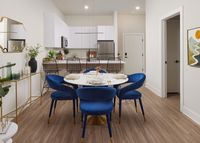 Chic apartment interior with a modern kitchen and dining area featuring blue velvet chairs, a marble table, and elegant decor.