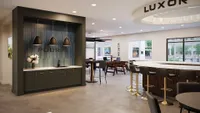 Modern communal space with a sleek bar area, elegant pendant lighting, and natural light pouring in through large windows.