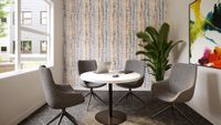 Contemporary dining area with stylish gray chairs, a round white table, vibrant artwork, and a lush plant by a bright window.