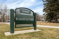 Barnum Park entrance sign in Denver, surrounded by grass and trees.