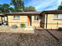 Charming brick exterior of a cozy home with a welcoming open door, surrounded by a low-maintenance rock garden and lush greenery.