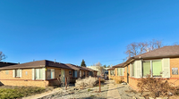 Charming brick duplex units with large windows and a sunny walkway, surrounded by a clear blue sky and peaceful landscaping.