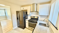 Modern kitchen with sleek white cabinets, stainless steel appliances, and elegant tile flooring leading into a bright living area.