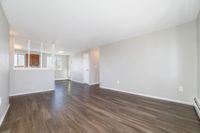 Bright and inviting living space with elegant laminate flooring and a partial view into the kitchen, showcasing modern design and ample natural light.