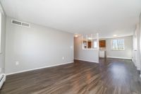 Bright and spacious living area with elegant wood flooring, large windows offering natural light, and a modern, partially open kitchen with sleek cabinetry.