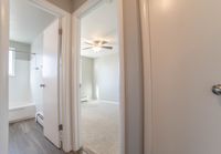 Inviting hallway view showcasing a bright and airy bedroom with soft carpet and a ceiling fan, adjacent to a modern bathroom with sleek floors.