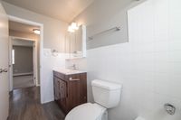 Bright and modern bathroom with elegant fixtures, a sleek wooden vanity, and pristine white tiles, offering a fresh and inviting atmosphere.