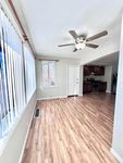 Bright and inviting living area with elegant wood flooring and modern ceiling fan, featuring large windows with vertical blinds in a contemporary open layout.
