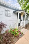 Charming home entrance with vibrant flowers, elegant siding, and welcoming porch under a clear blue sky.