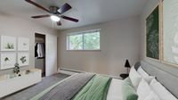 Inviting bedroom with a modern ceiling fan, large window, stylish wall art, and organized closet space with lush tree view.