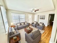 Bright and inviting living room featuring elegant gray sofas, cozy armchairs, wooden floors, and abundant natural light.