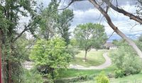 Scenic view of lush green parkland with winding walkway, framed by tall trees under a vibrant, cloudy sky.