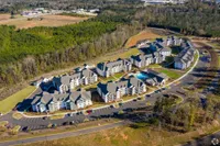 Aerial view of a modern apartment complex with lush surroundings, a central pool, and ample parking.