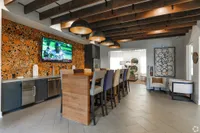 Stylish communal lounge with modern wooden decor, high chairs at a bar, and plush seating, ideal for social gatherings.
