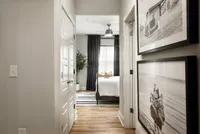 Corridor view leading to a bright bedroom with elegant decor, featuring framed wall art and wooden flooring.
