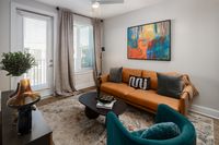Contemporary living room with a stylish tan sofa, vibrant abstract wall art, and elegant decor accents under natural light from large windows.