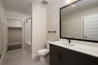 Modern bathroom featuring sleek black cabinetry, elegant white countertops, a large mirror, and a spacious walk-in closet.