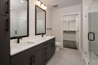 Elegant modern bathroom featuring dual sinks, large mirrors, and a sleek walk-in shower with glass doors, leading to a spacious walk-in closet.