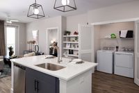 Modern and elegant apartment interior showcasing a chic kitchen island, open living area, and convenient in-unit laundry with stylish shelving accents.