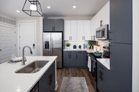 Modern kitchen with sleek cabinetry, stainless steel appliances, and elegant white countertops, featuring stylish pendant lighting and hardwood floors.