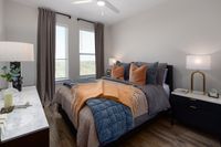 Elegant bedroom with a cozy ambiance featuring a plush bed with pillows and throws, modern nightstands, and chic décor elements. Natural light fills the space through large windows, highlighting the stylish wooden flooring.