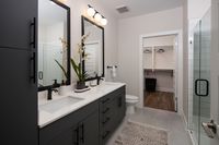 Elegant and modern bathroom with dual sinks, large mirrors, and a bright walk-in closet, featuring stylish black cabinetry and thoughtful decor.
