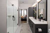 Elegant modern bathroom with sleek double vanity, spacious glass shower, and view into a cozy bedroom.