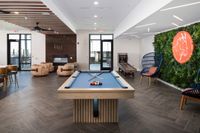 Chic apartment lounge with a modern pool table, cozy seating by a sleek fireplace, and vibrant greenery on the wall, designed for relaxation and entertainment.