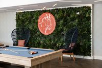 Chic recreational area with a modern billiards table, stylish rattan chairs, and a lush green wall featuring a striking art piece.