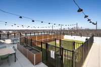 Charming rooftop patio with string lights, cozy seating, and stunning city views on a bright day.