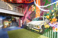 Vibrant urban art space featuring colorful graffiti with a classic car mural, lush greenery, and a chic modern staircase.