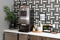 Sleek kitchen corner featuring a modern coffee machine, stylish geometric backsplash, and an elegant countertop setup with cups and condiments.