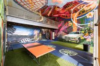 Vibrant indoor space featuring colorful murals, an orange ping pong table, and green artificial grass, creating a playful and artistic atmosphere.
