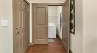 Inviting apartment hallway with elegant wooden flooring leading to a convenient laundry room with modern appliances.