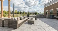 Charming outdoor patio featuring comfortable wicker seating, elegant fire pit, string lighting, and a built-in grill, perfect for entertaining.