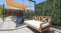 Modern outdoor patio featuring a stylish wooden swing, elegant shade sails, and vibrant greenery for a relaxing vibe.