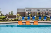 Elegant apartment complex with a sparkling pool, surrounded by vibrant blue and orange lounge chairs, offering a relaxing urban oasis.