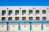 Modern apartment complex with a sleek design, featuring multiple balconies and ground-level garages under a clear blue sky.