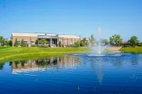 Charming community center overlooking a picturesque pond with a vibrant fountain and lush green surroundings.